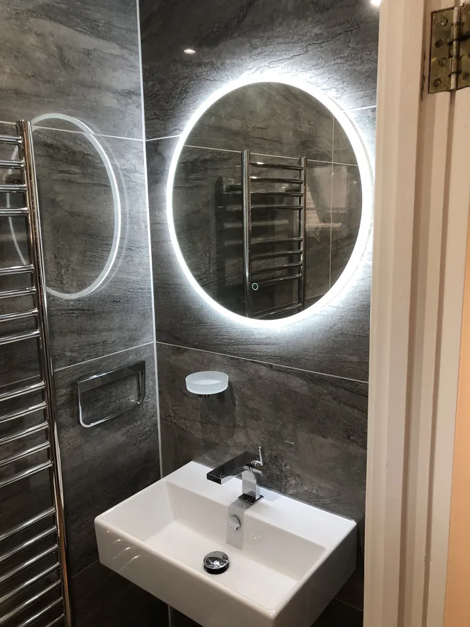 Dark stone-effect tiling with a backlit round mirror and basin