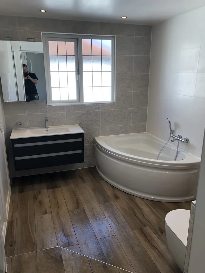 Corner bath with wood-effect floor tiles and grey wall tiling