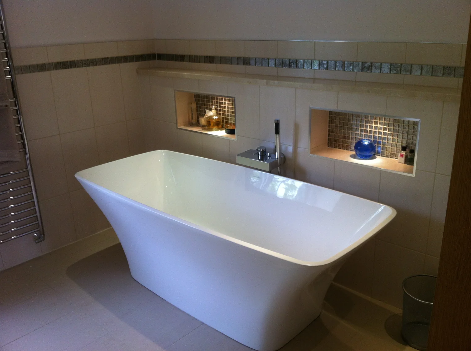 Freestanding bath beside tiled recessed niches lit from within
